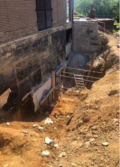 Grande fouille le long d’un bâtiment ancien avec parois étayées, gravats et échelle d’accès, réalisée dans le cadre de travaux d’étude de sol et d’assainissement des sols supervisés par Aquaconseil.